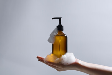 A hand holds an amber-colored soap dispenser covered with suds