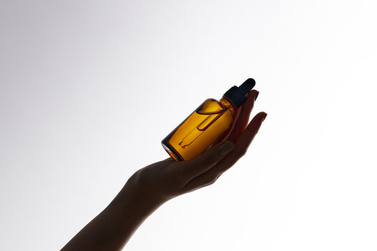 A graceful hand presents a bottle of essential oil against a cle