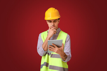 Young male engineer with tablet computer on red background