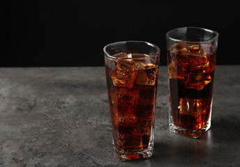 Cold cola with ice cubes in glasses on grey table. Space for text