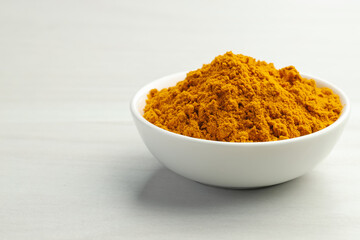 Turmeric powder in bowl on white table, closeup. Space for text