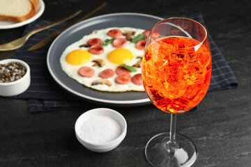 Tasty brunch. Aperol cocktail, delicious fried eggs with sausage served on black table, closeup