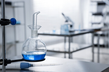Flask with blue liquid on retort stand in laboratory, closeup. Space for text