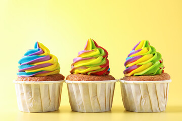 Tasty cupcakes with colorful cream on yellow background, closeup