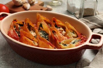 Delicious conchiglie pasta with ricotta cheese, spinach and tomato sauce in baking dish on gray textured table, closeup