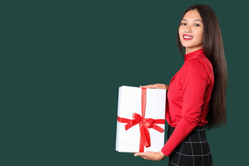 Beautiful young Asian woman with gift box on green background