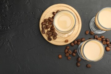Coffee cream liqueur in glasses and beans on black table, flat lay. Space for text