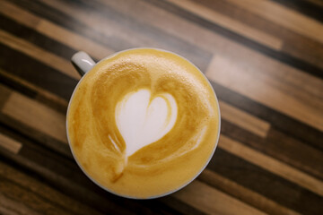 Cappuccino with a heart on the foam stands in a cup on a wooden table. Top view