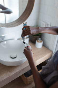 Woman applying toothpaste from tube on toothbrush
