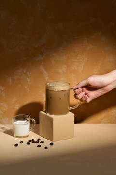 Hand Reaching for a Creamy Iced Coffee with Milk and Beans