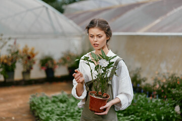 A young woman planting flowers in a greenhouse, showcasing a mix of emotions and passion for...