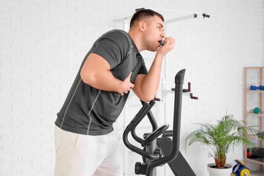 Sporty young man using inhaler on exercise bike in gym
