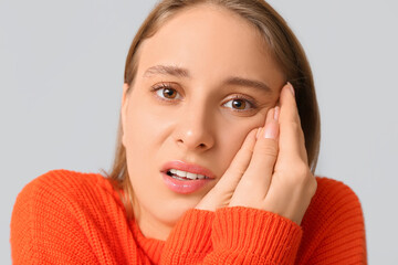 Beautiful young woman suffering from toothache on grey background, closeup