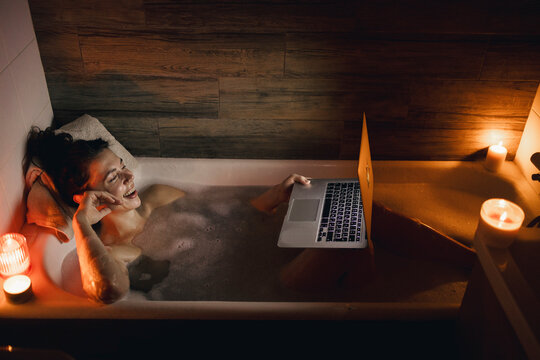 Cheerful woman watching movie on laptop in bathroom