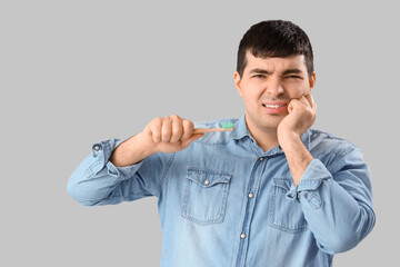 Young man with brush suffering from toothache on light background, closeup
