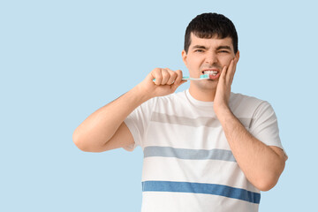 Young man with brush suffering from toothache on blue background