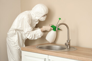 Female worker of cleaning service removing mold from beige wall over sink in kitchen
