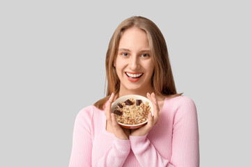 Happy young woman with bowl of healthy oatmeal on grey background