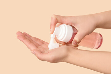 Female hands with bottle of sanitizer product on beige background