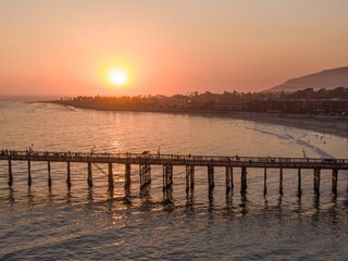 Obraz premium Aerial view of people enjoying the sunset on the Ventura Pier in California, USA. Tourists and locals visit the pier for recreation and scenic views.