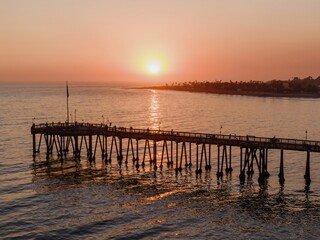 Fototapeta premium People stroll along the pier in Ventura, California, USA, enjoying the sunset. The sun reflects on the water, creating a peaceful and scenic view.