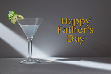 Happy Father's Day text in yellow with a martini on a grey background with a beam of light.