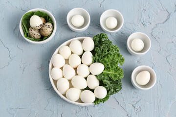 Plate and bowls of fresh boiled quail eggs with lettuce on blue background