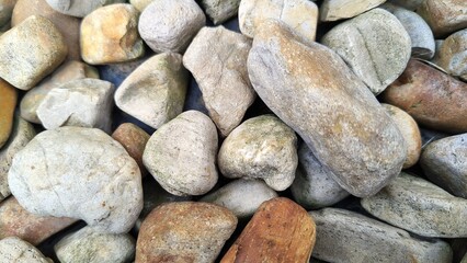Close-up of smooth river stones in earthy tones, ranging from beige to brown, with dried leaves in between. The stones have a weathered texture
