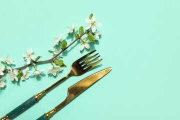 Golden cutlery with blossoming branch on turquoise background