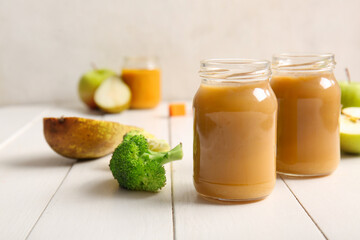 Glass jars of healthy baby puree and ingredients on light wooden table
