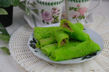 kue dadar gulung, a dessert made of glutinous rice, coconut and palm sugar. also known as ketayap served in plate on wooden board. wooden background. high angle. street food.