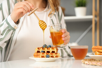 Woman adding sweet honey to sweet waffles in kitchen