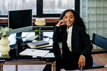 Confident smiling businesswoman leaning at table in modern office