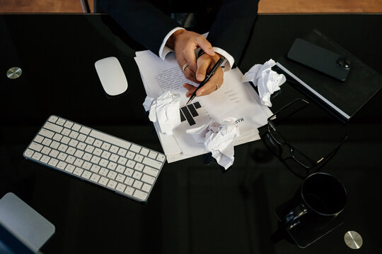 Hands holding pen over crumpled papers and documents, brainstorm