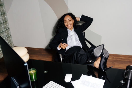 Relaxed businesswoman smiling at camera while using  smartphone