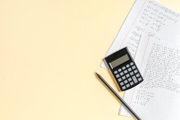 Copybook with handwritten maths formulas, pencil and calculator on yellow background