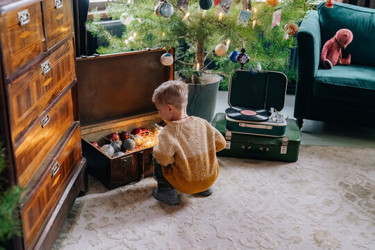 Child exploring a treasure chest of holiday decorations indoors