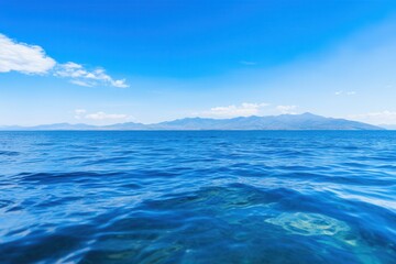 Serene Blue Ocean Waves Under Clear Sky with Distant Mountains View