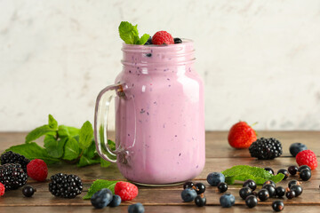 Mason jar of fresh smoothie with different berries and mint on wooden table
