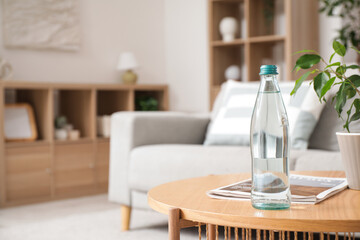 Bottle of water with magazine and plant on table in living room, closeup