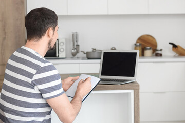 Obraz premium Young male teacher with laptop and notebook giving online lesson at home
