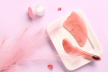 Plate with facial massage tools and jar of cosmetic product on pink background