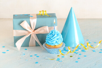 Sweet Birthday cupcake with burning candle, gift box and party hat on light blue table