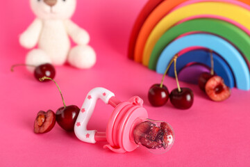 Baby nibbler with sweet cherry and toys on color background