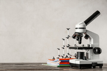 Modern microscope with molecular model and copybooks on wooden table against white grunge background
