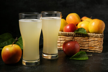 Glasses of fresh apple kvass and wicker basket with fruits on black background