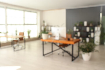 Blurred view of office with desks, shelf units and green plants