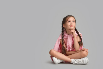 Thoughtful little girl sitting on light background
