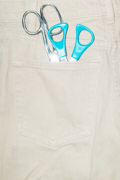 Pairs of cutting scissors in pocket of denim jeans with flash