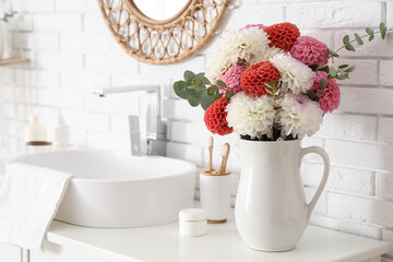 Vase with beautiful dahlia flowers near sink in stylish light bathroom